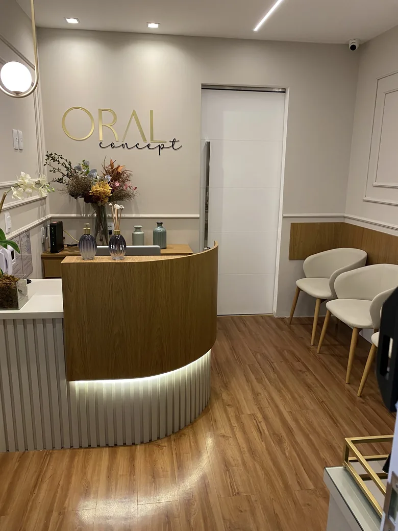 Recepção da clínica com balcão de madeira iluminado, poltronas claras e o nome Oral Concept na parede