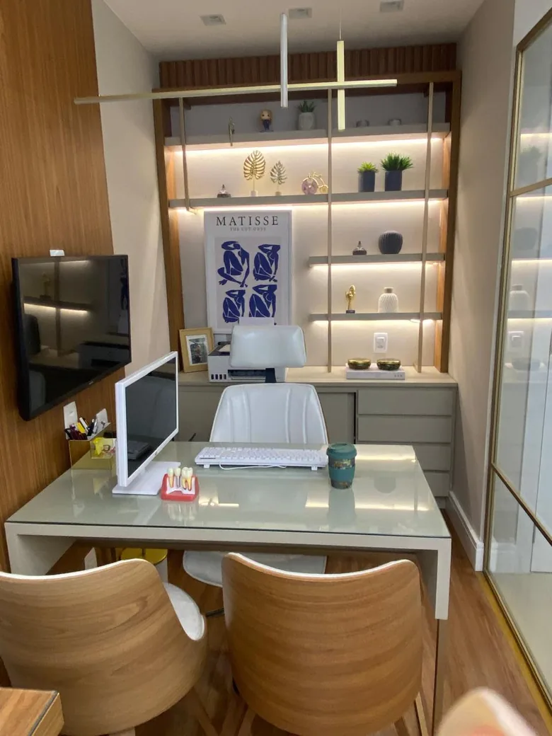 Sala com mesa de atendimento, cadeiras de madeira e estante iluminada com objetos decorativos