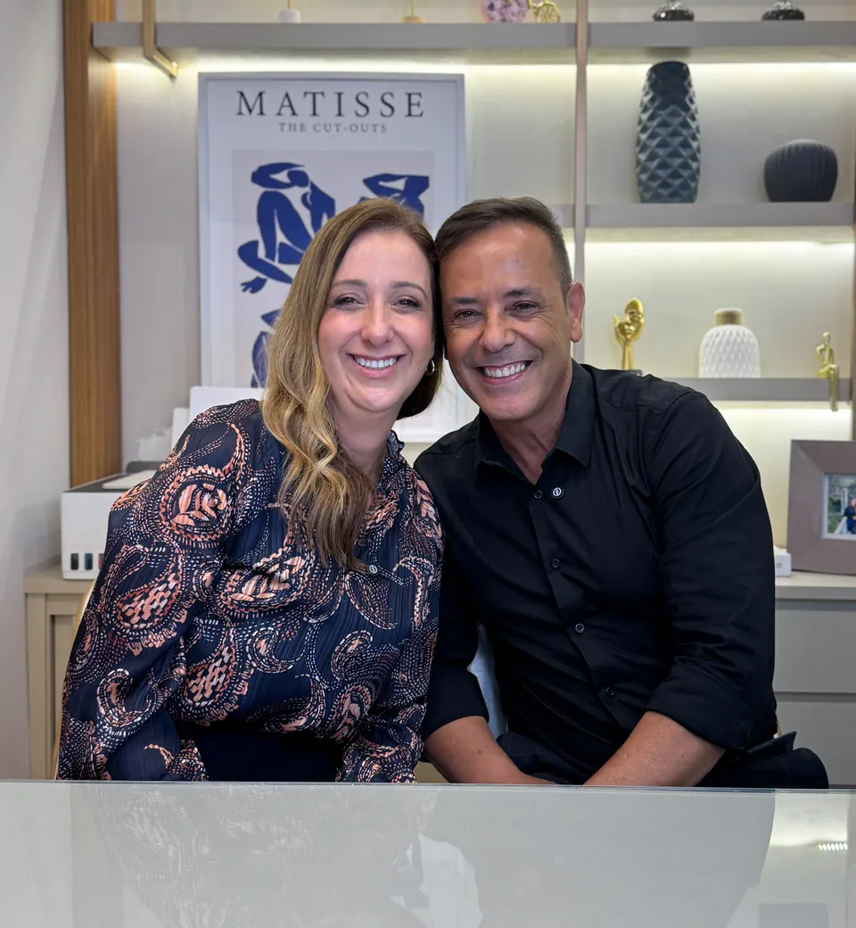 Dra. Micheli Bragantini e André, sócios da Oral Concept, sorrindo lado a lado na sala de atendimento da clínica